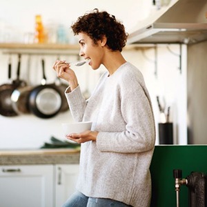 Woman standing in kitchen, eating from a bowl
