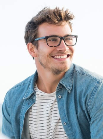 Young man with glasses and denim shirt smiling outdoors