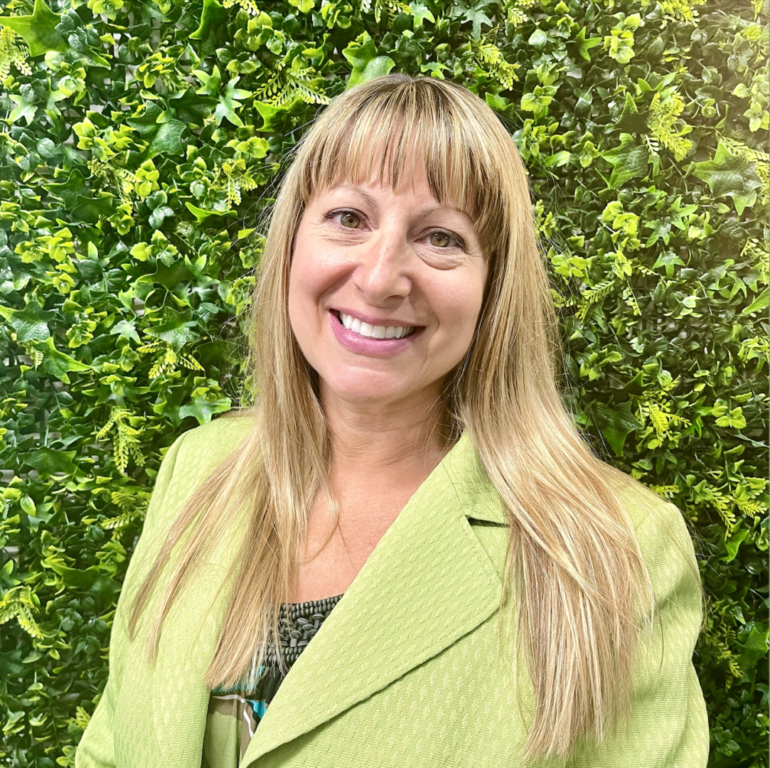 A woman in a green jacket standing next to a wall.