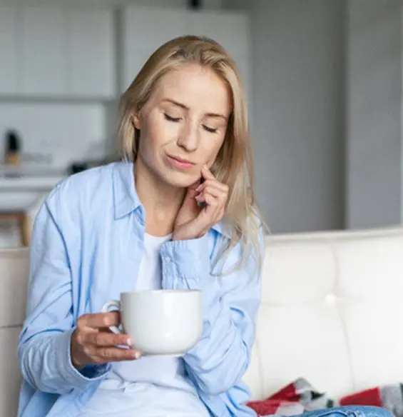 A woman sitting on the couch holding a cup of coffee.