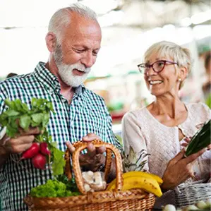 A man and woman holding vegetables in front of a basket.