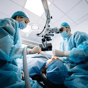 Two surgeons in blue gowns performing surgery on a patient.