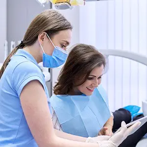 Two women in blue shirts and masks looking at a tablet.