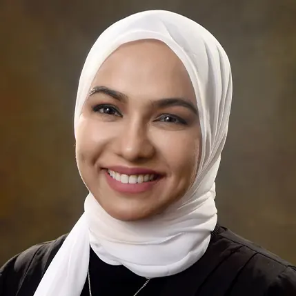 A woman wearing a white head scarf and smiling.