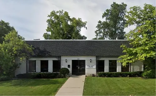 A large white building with black roof and trees in the background.