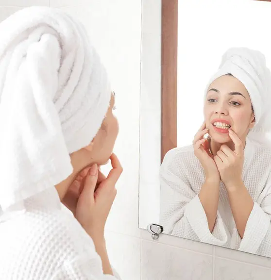 A woman in white robe looking at her reflection in the mirror.