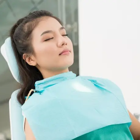 A woman sitting in the dentist chair with her eyes closed.