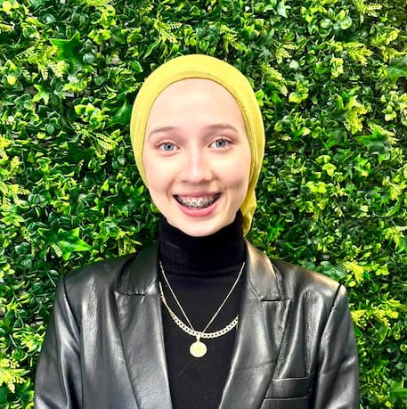 A woman wearing a yellow head covering and black jacket.