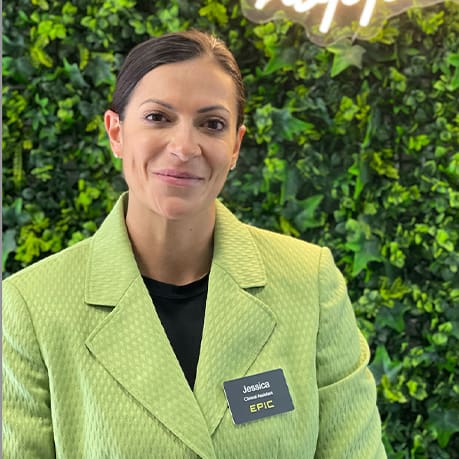 A woman in a green jacket standing next to a wall.